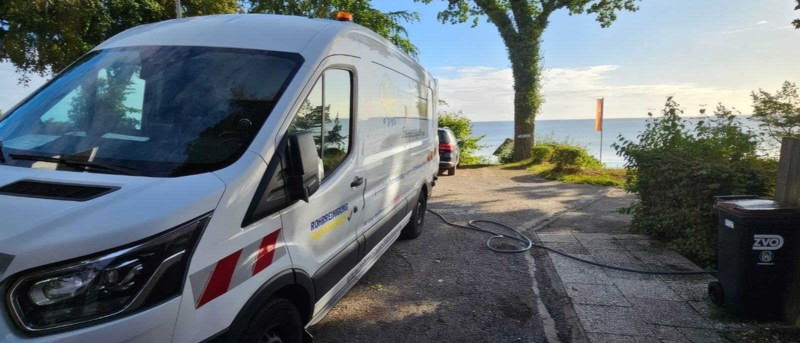 Transporter von Rohrreinigung Falkenhagen auf einem Weg an der Ostsee, ein Schlauch führt zur Leitung, im Hintergrund das Meer
