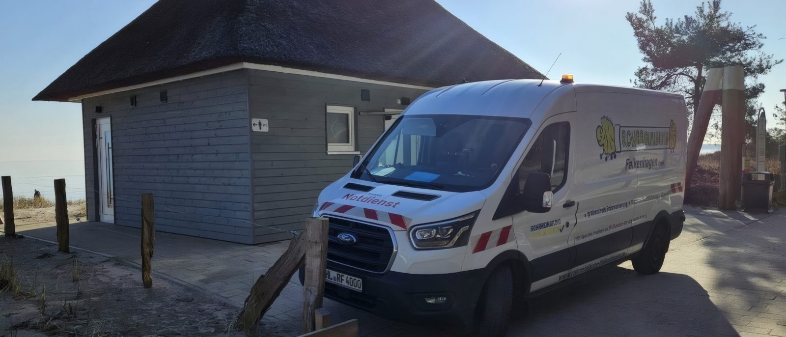 Transporter von Rohrreinigung Falkenhagen neben der reetgedeckten öffentlichen WC-Anlage am Strand von Scharbeutz