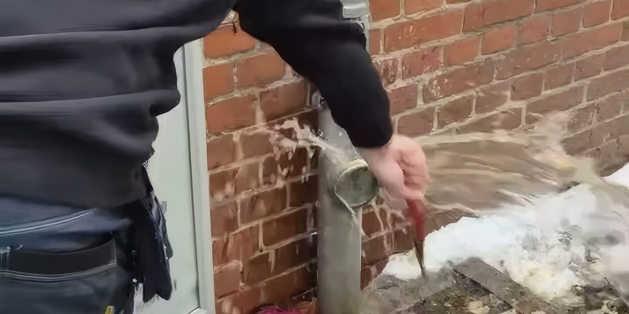 Mitarbeiter von Rohrreinigung Falkenhagen öffnet die Reinigungsöffnung an einem Regenfallrohr vor einer Klinkerwand, Wasser tritt aus