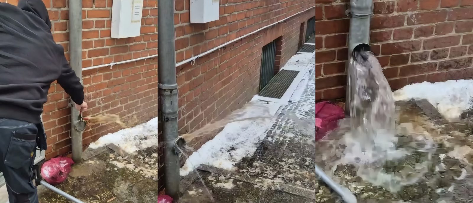 Regenfallrohr an einer Klinkerwand im Winter, ein Mitarbeiter öffnet die Reinigungsöffnung und Wasser tritt aus